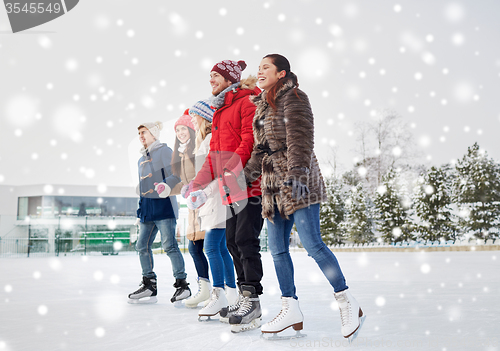 Image of happy friends ice skating on rink outdoors