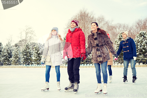 Image of happy friends ice skating on rink outdoors