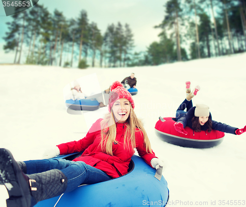 Image of group of happy friends sliding down on snow tubes