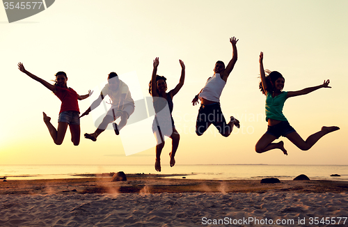 Image of smiling friends dancing and jumping on beach