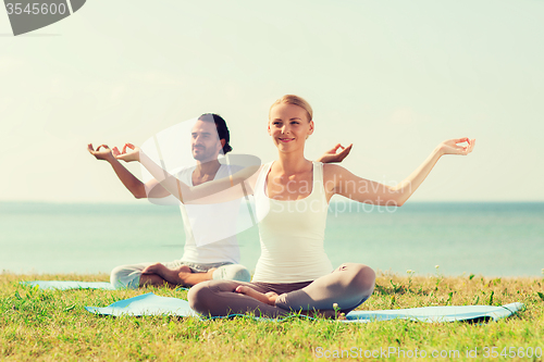 Image of smiling couple making yoga exercises outdoors