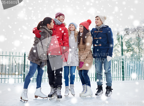 Image of happy friends ice skating on rink outdoors