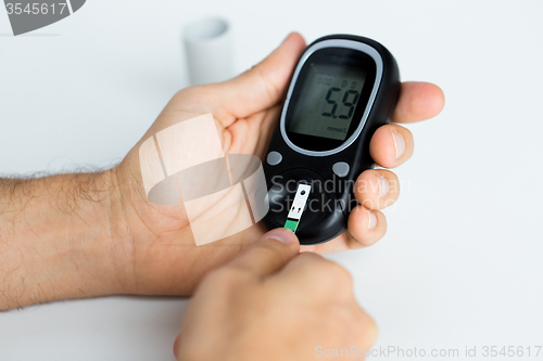 Image of close up of man checking blood sugar by glucometer