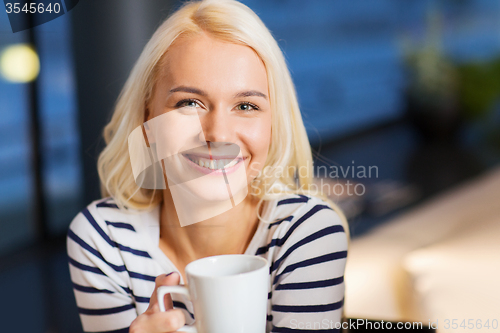 Image of smiling young woman drinking coffee at cafe