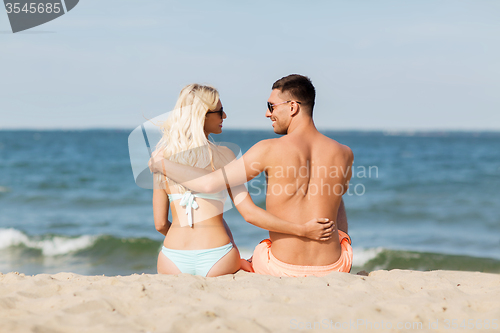 Image of happy couple in swimwear sitting on summer beach