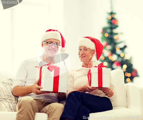 Image of happy senior couple in santa hats with gift boxes