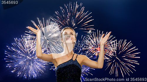 Image of smiling woman raising hands up over firework