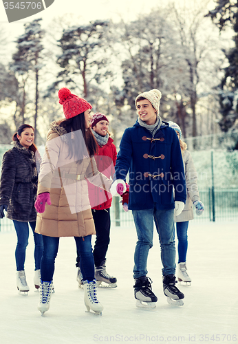 Image of happy friends ice skating on rink outdoors