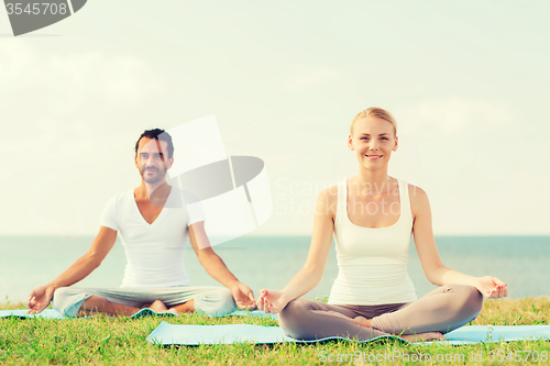 Image of smiling couple making yoga exercises outdoors