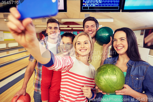 Image of happy friends with smartphone in bowling club