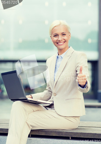 Image of smiling businesswoman working with laptop outdoors