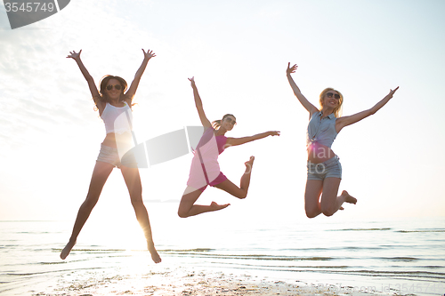 Image of happy female friends dancing and jumping on beach