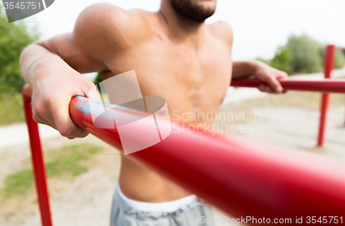 Image of young man exercising on parallel bars outdoors