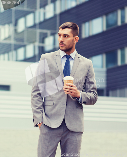 Image of young serious businessman with paper cup outdoors