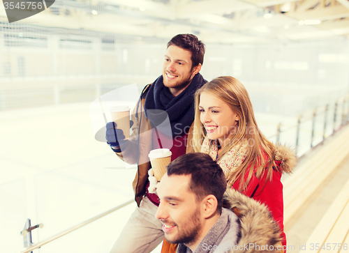 Image of happy friends with coffee cups on skating rink