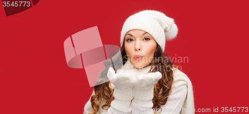 Image of happy woman in winter clothes blowing on palms