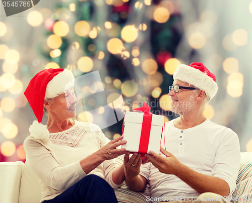 Image of happy senior couple in santa hats with gift box