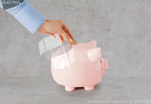 Image of close up of hand putting coin to piggy bank