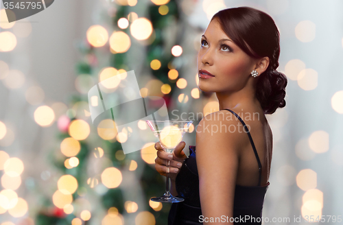 Image of woman with cocktail over christmas tree lights