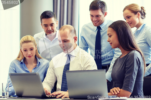 Image of smiling businesspeople with laptops in office