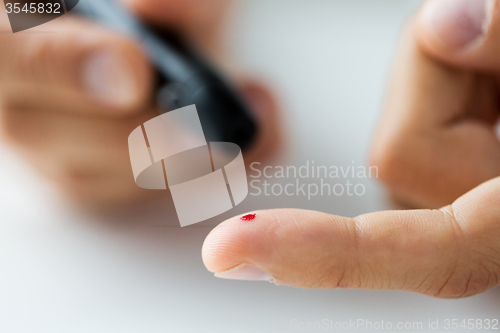 Image of close up of male finger with blood and glucometer