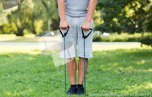 Image of young man exercising with expander in summer park