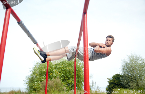 Image of young man doing sit up on parallel bars outdoors