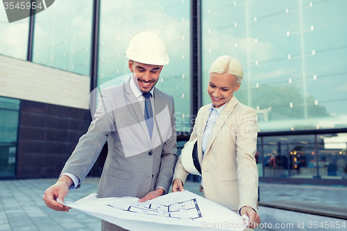 Image of smiling businessmen with blueprint and helmets