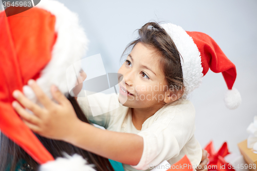 Image of happy mother and little girl in santa hats at home