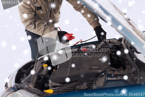 Image of closeup of man under bonnet with starter cables