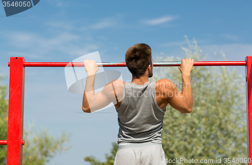 Image of young man exercising on horizontal bar outdoors