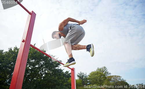 Image of young man jumping on horizontal bar outdoors