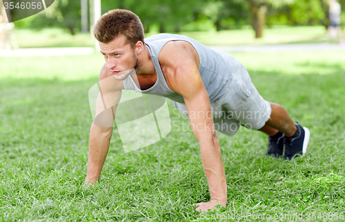 Image of young man doing push ups on grass in summer park