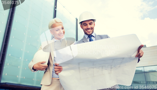 Image of smiling businessmen with blueprint and helmets