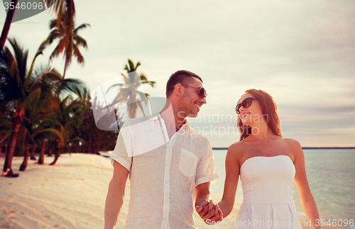 Image of smiling couple in sunglasses walking on beach