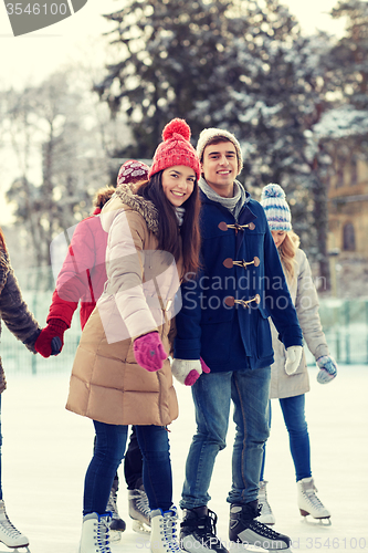 Image of happy friends ice skating on rink outdoors