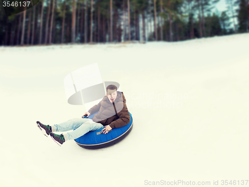 Image of happy young man sliding down on snow tube