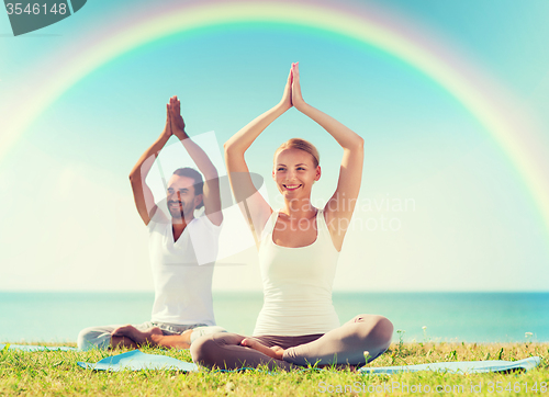 Image of smiling couple making yoga exercises outdoors