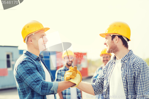 Image of group of smiling builders in hardhats outdoors