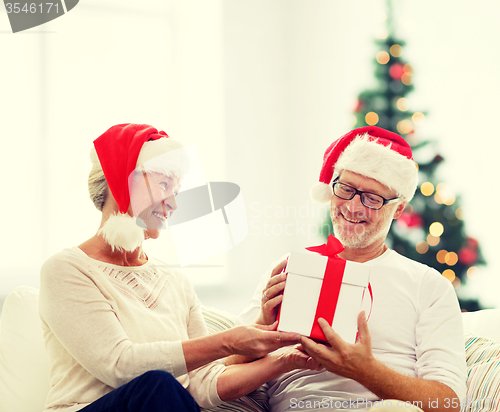 Image of happy senior couple in santa hats with gift box