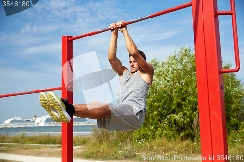 Image of young man exercising on horizontal bar outdoors