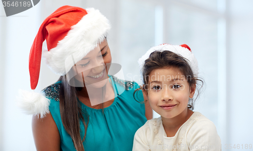 Image of happy mother and little girl in santa hats at home