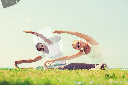 Image of smiling couple making yoga exercises outdoors