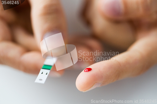 Image of close up of male finger with blood and test stripe