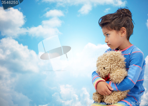 Image of sad little girl with teddy bear toy over blue sky