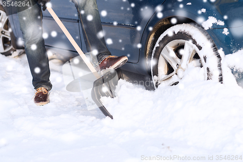 Image of closeup of man digging snow with shovel near car