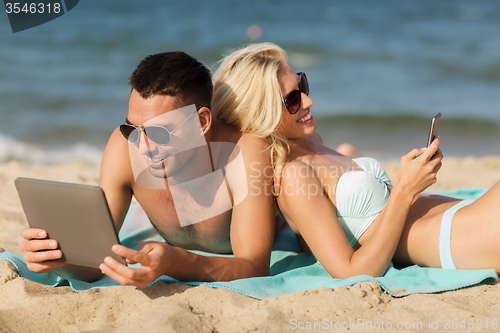 Image of happy couple with tablet pc sunbathing on beach