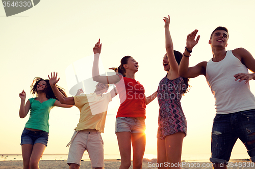 Image of smiling friends dancing on summer beach