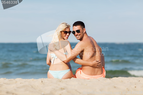 Image of happy couple in swimwear sitting on summer beach