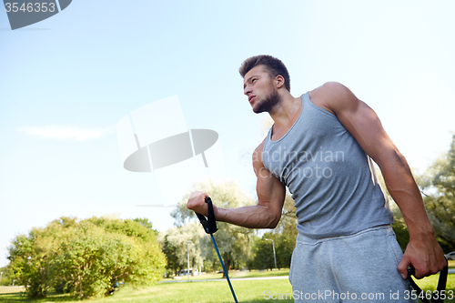 Image of young man exercising with expander in summer park